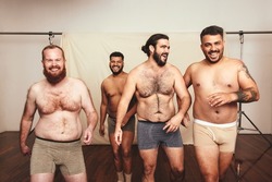 Laughter is the best body medicine. Group of self-confident young men laughing cheerfully while wearing underwear in a modern studio. Four shirtless young men embracing their natural bodies.
