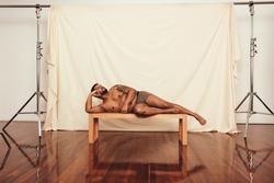 Comfortable in underwear. Body positive young man looking relaxed while lying shirtless on a bench in a modern studio. Self-confident young man embracing his natural body.