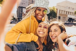 Trio of friends taking a selfie together. Group of multiethnic female friends having fun together outdoors. Cheerful generation z friends capturing their happy moments in the city.
