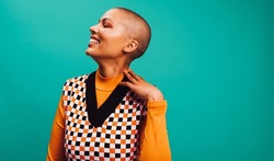 Confident short-haired woman smiling in a studio. Happy young woman standing with her eyes closed against a turquoise background. Fashionable young woman wearing a septum ring.