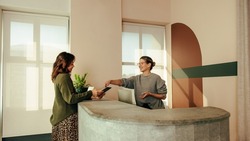 Carefree receptionist assisting a woman with signing in to an office. Friendly receptionist showing a woman where to sign on a digital tablet. Woman working at the front desk of a co-working space.