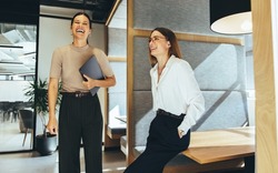 Female business professionals laughing cheerfully in an office. Two successful young businesswomen taking a short break while together in a modern workspace.