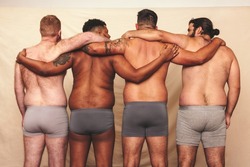 Embracing our natural bodies together. Rearview of a group of body positive men embracing each other while standing in underwear. Self-confident men flexing their natural bodies.