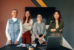 Successful female entrepreneurs smiling cheerfully while standing behind a table in a boardroom. Group of multicultural businesswomen working together in a modern office.