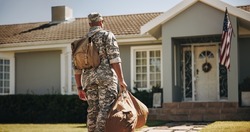 Patriotic young soldier walking towards his house with his luggage. Rearview of an American serviceman coming back home after serving in the military.