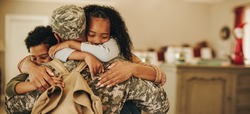 Soldier embracing his wife and kids on his homecoming. Serviceman receiving a warm welcome from his family after returning from deployment. Military family having an emotional reunion.