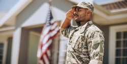 Patriotic young soldier saluting while standing outside his home. Member of the United States Marine Corps showing honour and respect on Veterans Day.
