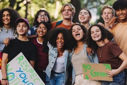 Group of multicultural teenagers smiling happily while standing together at a climate change protest. Diverse youth activists joining the global climate strike.
