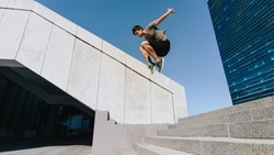 Young man jumping high over steps outdoors. Fit male free runner jumping over stairs in urban space.