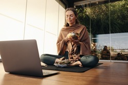 Ayurvedic healer meditating with a singing bowl and sage during an online holistic class. Woman performing a self-healing and purifying ceremony at home. Senior woman taking care of her ageing body.