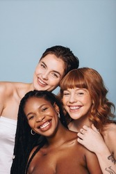 Happy women with different skin tones smiling at the camera in a studio. Group of body confident young women embracing their natural beauty. Three body positive young women standing together.