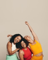 Three young women laughing happily as they stand together in a studio wearing sports clothing. Group of female friends celebrating their fit, healthy and sporty lifestyle.