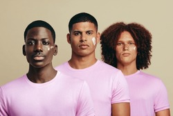 Portrait of three men standing together and looking at the camera with a beauty product on their faces. Confident young men with unique skin tones using a cosmetic cream in their skincare routine.