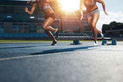 Sprinters starts out of the blocks on athletics racetrack with bright sunlight. Low section shot of female athletes starting a race in stadium with sunflare.