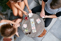 Top view of three young people playing cards at sidewalk cafe. Young people sitting around a coffee table and playing card game.