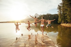Portrait of young friends jumping into the water from a jetty. Young people having fun at the lake on a summer day.