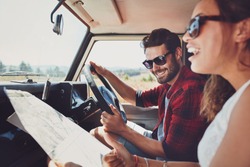 Happy young couple with a map in the car. Smiling man and woman using map on roadtrip.