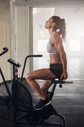 Side view shot of fitness woman spinning air bike at the gym. Fitness woman working out on exercise bike at the gym.