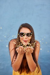 Portrait of happy young female model blowing confetti in the air over shining background
