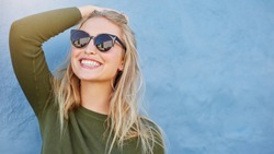 Close up shot of stylish young woman in sunglasses smiling against blue background. Beautiful female model with copy space.