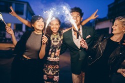 Group of friends holding sparklers out on street at night. Young men and women having night party with sparklers.