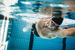 Fit swimmer training in the swimming pool. Professional male swimmer inside swimming pool.