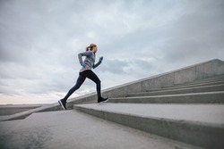 Full length shot of woman running on steps outdoors. Fitness female exercising in morning.