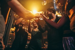 Low angle shot of group of friends enjoying drinks at bar together. Young people at nightclub toasting cocktails.