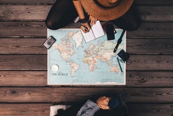 Man and woman planning vacation using a world map and other travel accessories. Woman noting the  discussion points in a small diary.