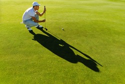 Pro golf player aiming shot with club on course. male golfer check line for putting golf ball on green grass.