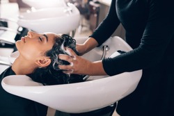 Woman applying shampoo and massaging hair of a customer. Woman having her hair washed in a hairdressing salon.