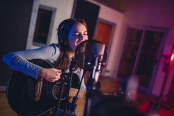 Female vocal artist singing in a recording studio with guitar. Woman singer singing a song and playing guitar.