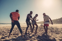 Young friends playing football on the sandy beach. African people enjoying a game of soccer on summer day.