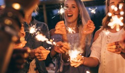 People at night holding sparklers. Group of friends enjoying with sparklers in evening.