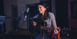 Female singer playing guitar and singing a song. Woman performing in a recording studio. Recording for her album.