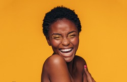Cheerful young african woman with vivid makeup on her eyes. Female model laughing against yellow background.