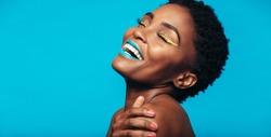 Close up of cheerful young woman with colorful makeup. Beauty portrait of female model with vivid makeup laughing on blue background.