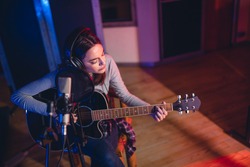 Woman artist playing guitar in a recording studio. Female singer performing a song in studio.