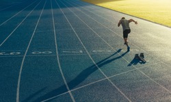 Athlete running on an all-weather running track alone. Runner sprinting on a blue rubberized running track starting off using a starting block.