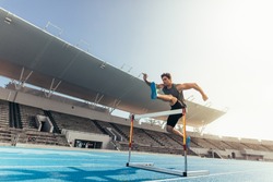 Runner jumping over an hurdle during track and field event. Athlete running a hurdle race in a stadium.