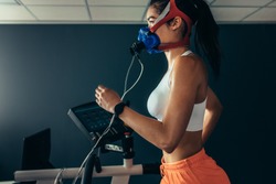 Side view of professional sportswoman with mask running on treadmill in gym. Female athlete in sports science lab measuring her performance and oxygen consumption.
