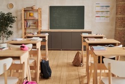Wide angle background image of wooden school desks in row facing blackboard in empty classroom, copy space