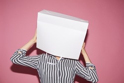 Anonymous woman in black and white shirt standing against pink wall and holding white paper bag over her head, shopping concept