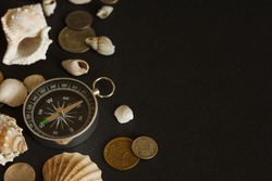 Still life with a compass, coins and shells. Dark background. Nautical theme. Top view travel or vacation concept. Traveler accessories on a dark background with blank space for text. Copy space