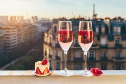 Paris luxury lifestyle. Pink champagne with rasberries in two glasses, traditional french cake with strawberries on a balcony with a view on rooftops and Eiffel Tower on the sunset