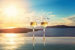 Two champagne glasses on the edge of infinity swimming pool at sunset, Santorini island. Drink, celebrate, vacation and summer concept.