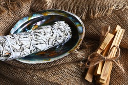 An image of white sage smudge sticks in an abalone shell with a burlap background. 