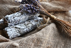 An image of white sage smudge sticks and dried lavender flowers on vintage burlap cloth. 