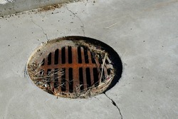 An image of a old rusted covered storm drainage lid with cracked pavement. 