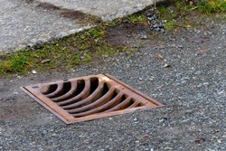 An image of an old rusted metal storm drain cover on a paved street.